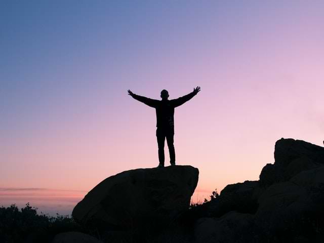 man on a boulder with arms spread wide