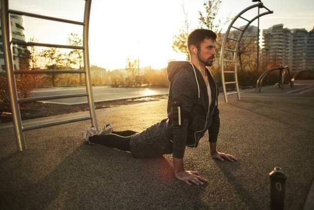 man doing stretch in park sun rising