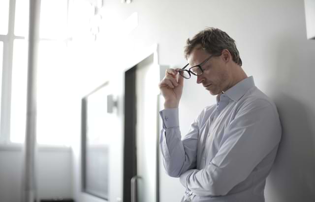 Man Thinking with Glasses Off Against the Wall