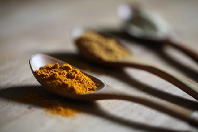 tumeric in a spoon along with other spices on a table
