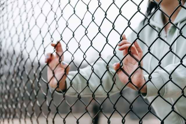 woman facing fence with hands