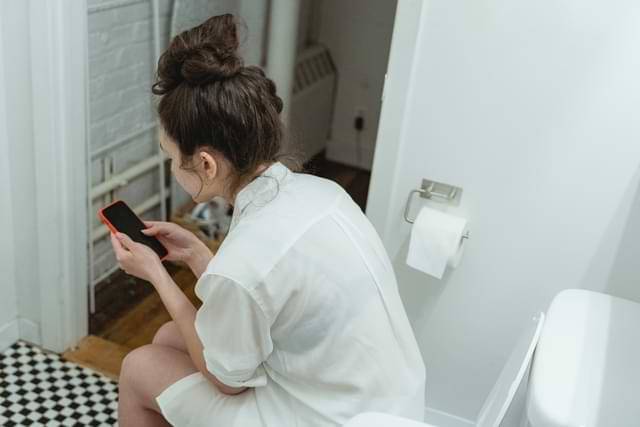 Woman Using Phone on Toilet